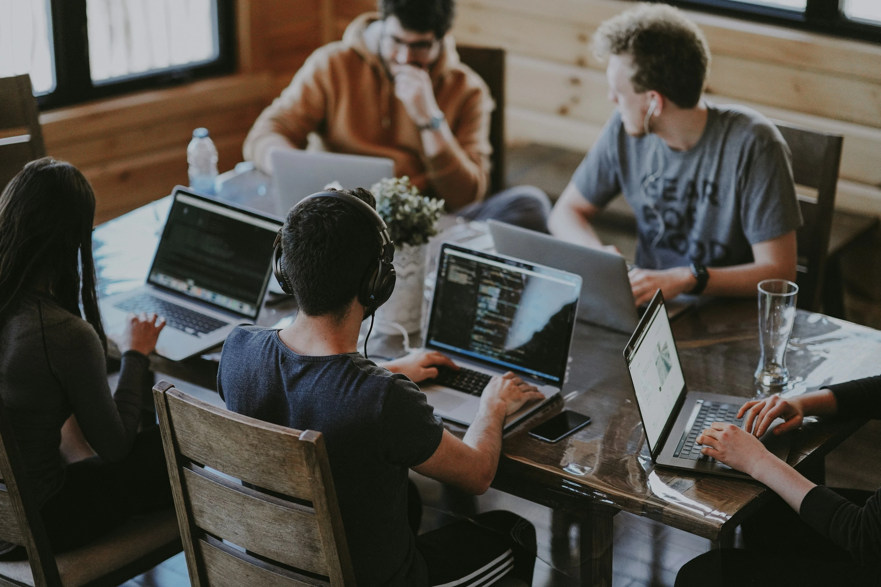 Team collaboration - developers working together around a wooden table with laptops in a bright, modern workspace